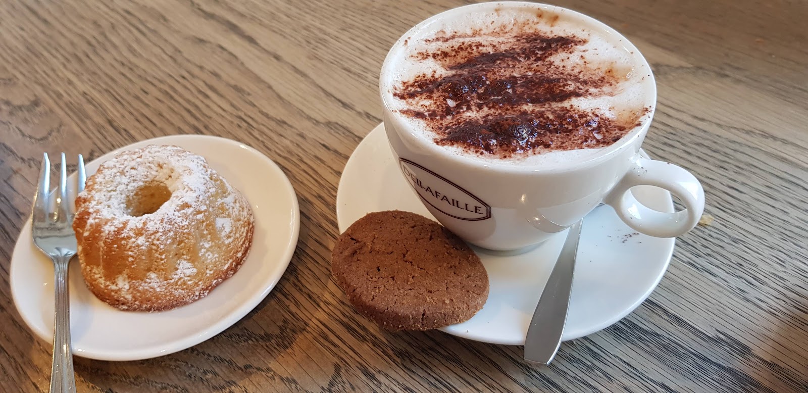 Cappuccino met cacao en een vers koffiekoekje op tafel bij Bakkerij Dellafaille