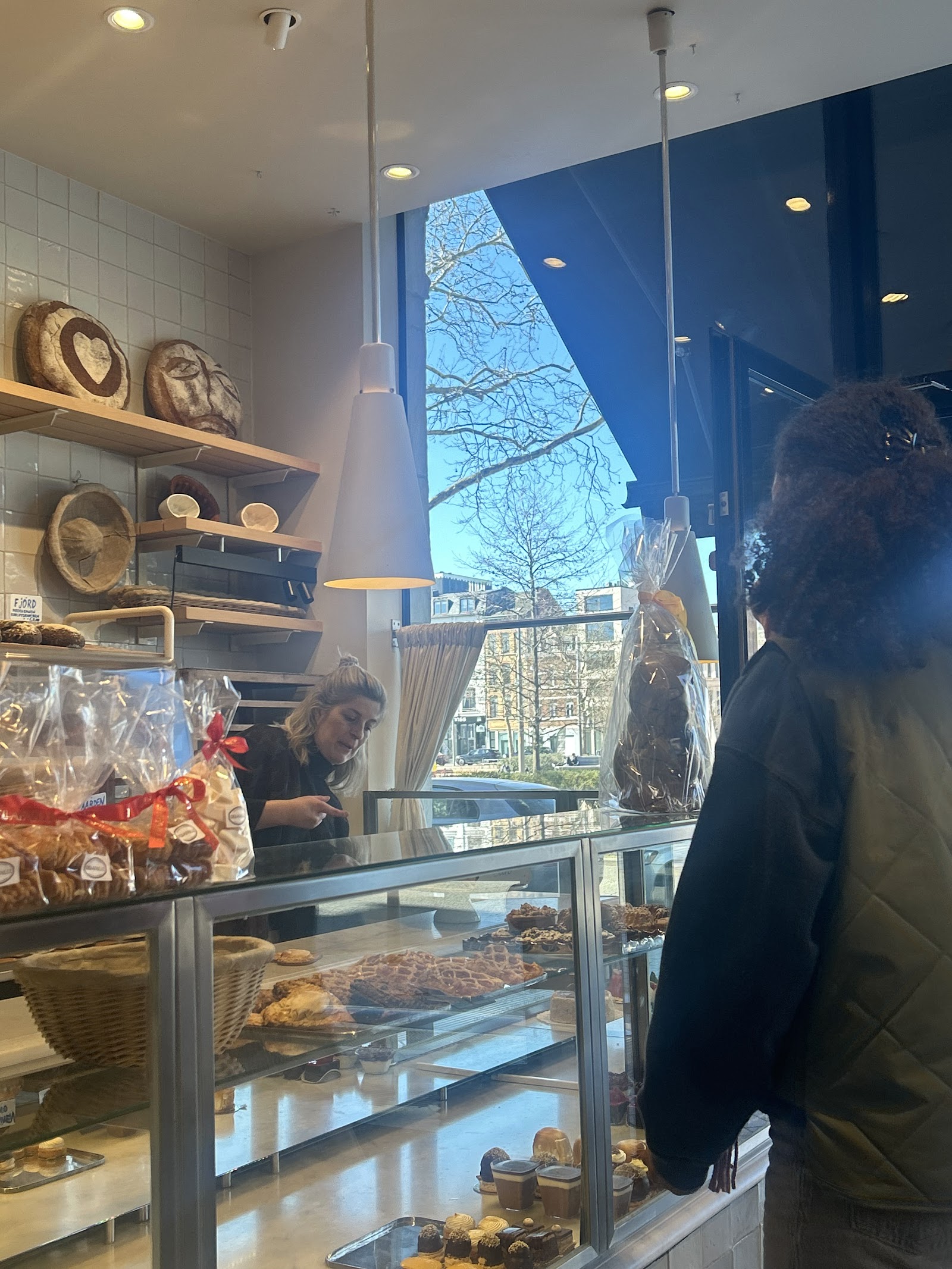 Bakker aan de toonbank van Bakkerij Dellafaille, met zuurdesembroden op het rek en daglicht door het raam